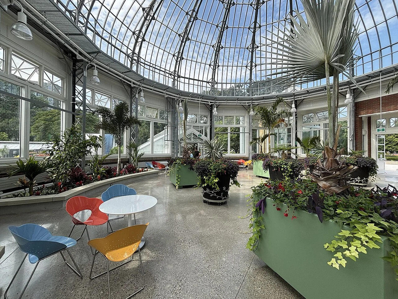 Potted palms, planting beds and seating beneath the glass dome of the restored Palm House at Allan Gardens.