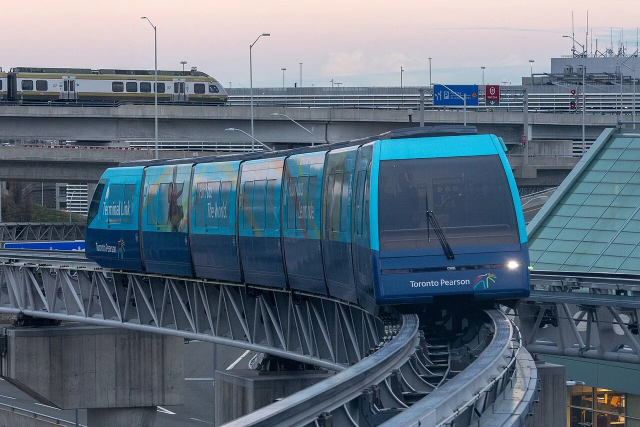 A blue Terminal Link train at Pearson Airport, with an UP Express train on a separate track behind it.