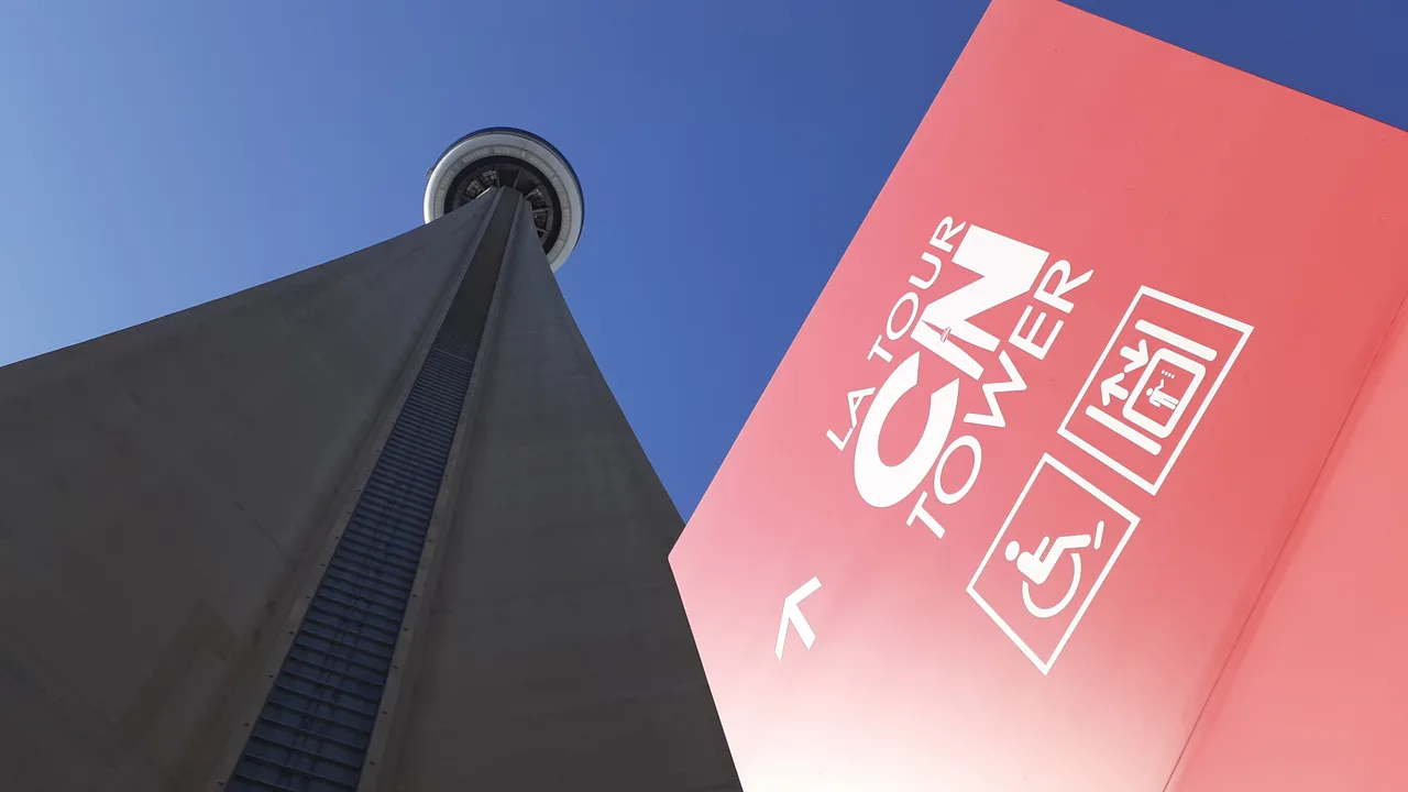 CN Tower viewed from its base beside a red entrance sign.