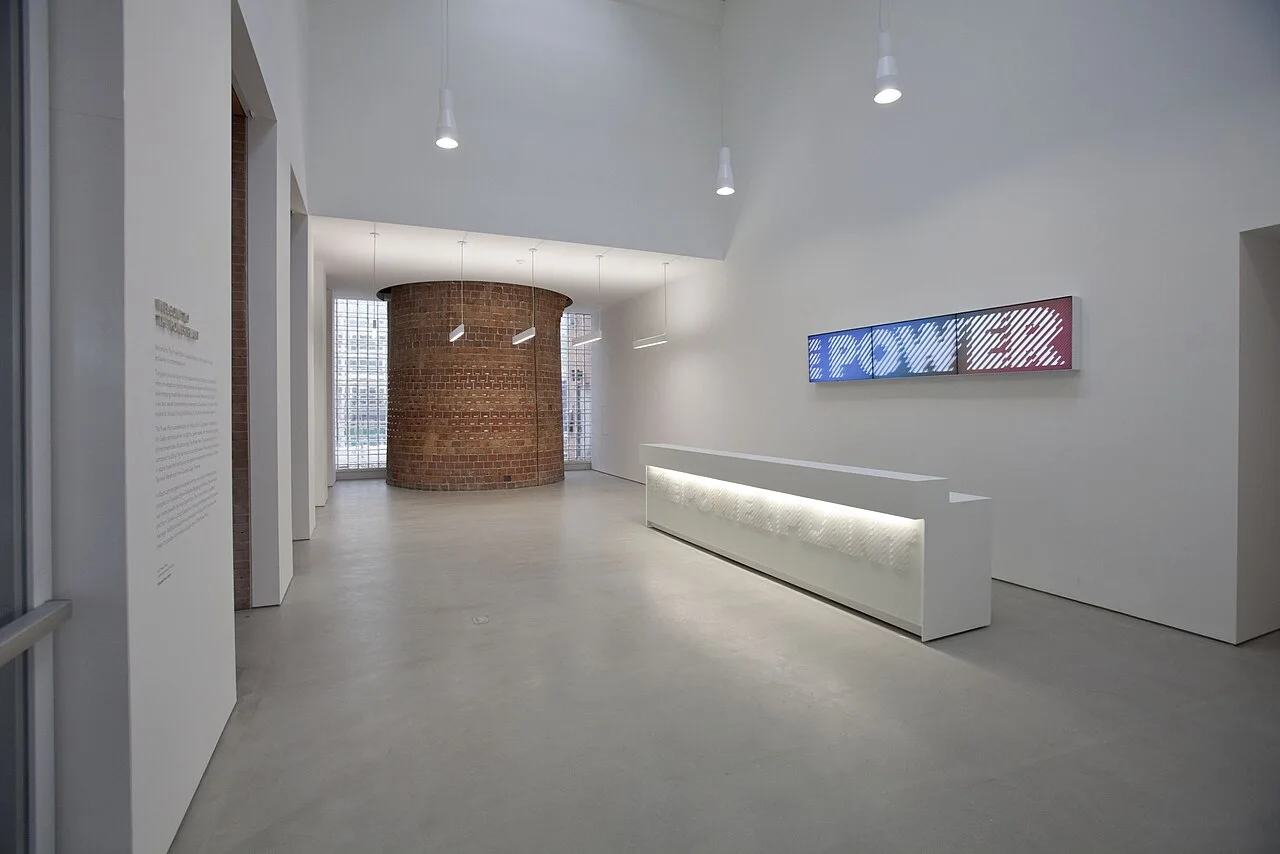 White lobby at The Power Plant with a reception desk and exposed brick chimney base.