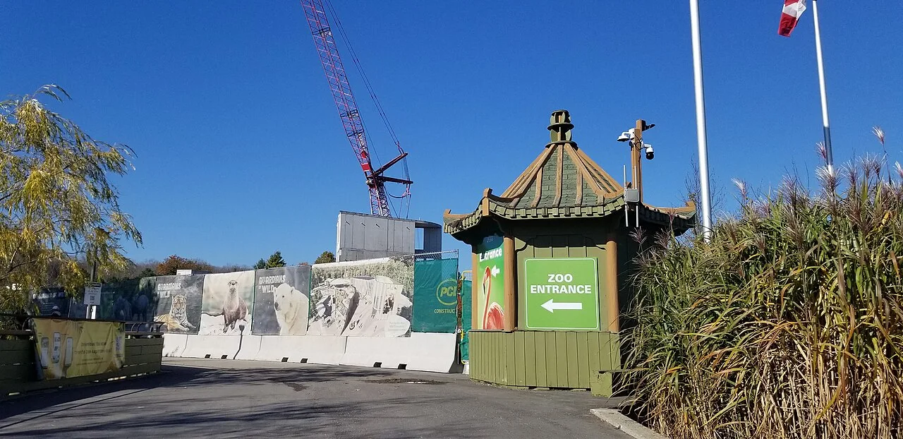 Toronto Zoo entrance sign beside construction hoarding and planted grounds.