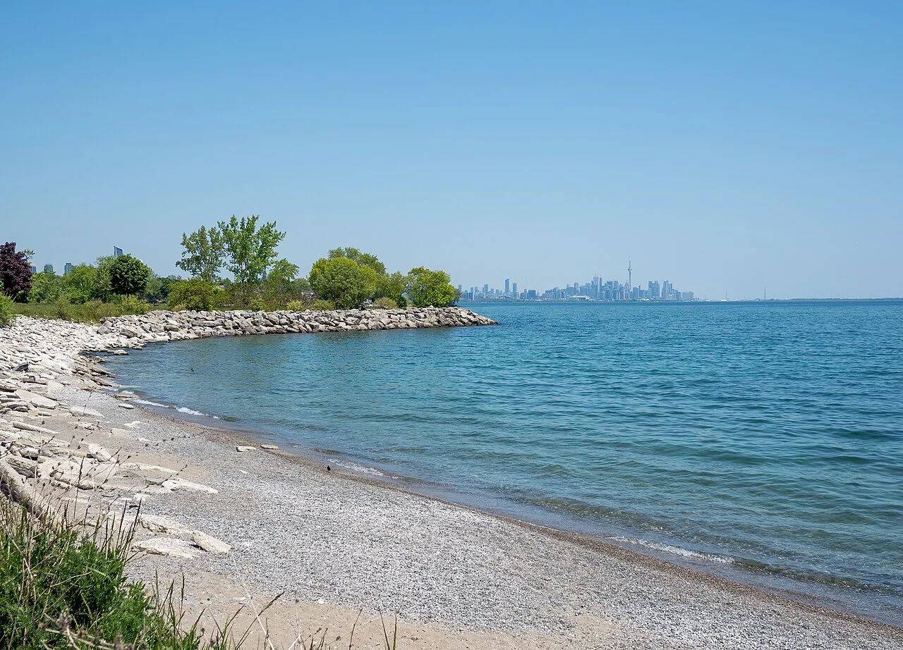 Rocky shoreline and trees at Colonel Samuel Smith Park, with Toronto’s skyline beyond.