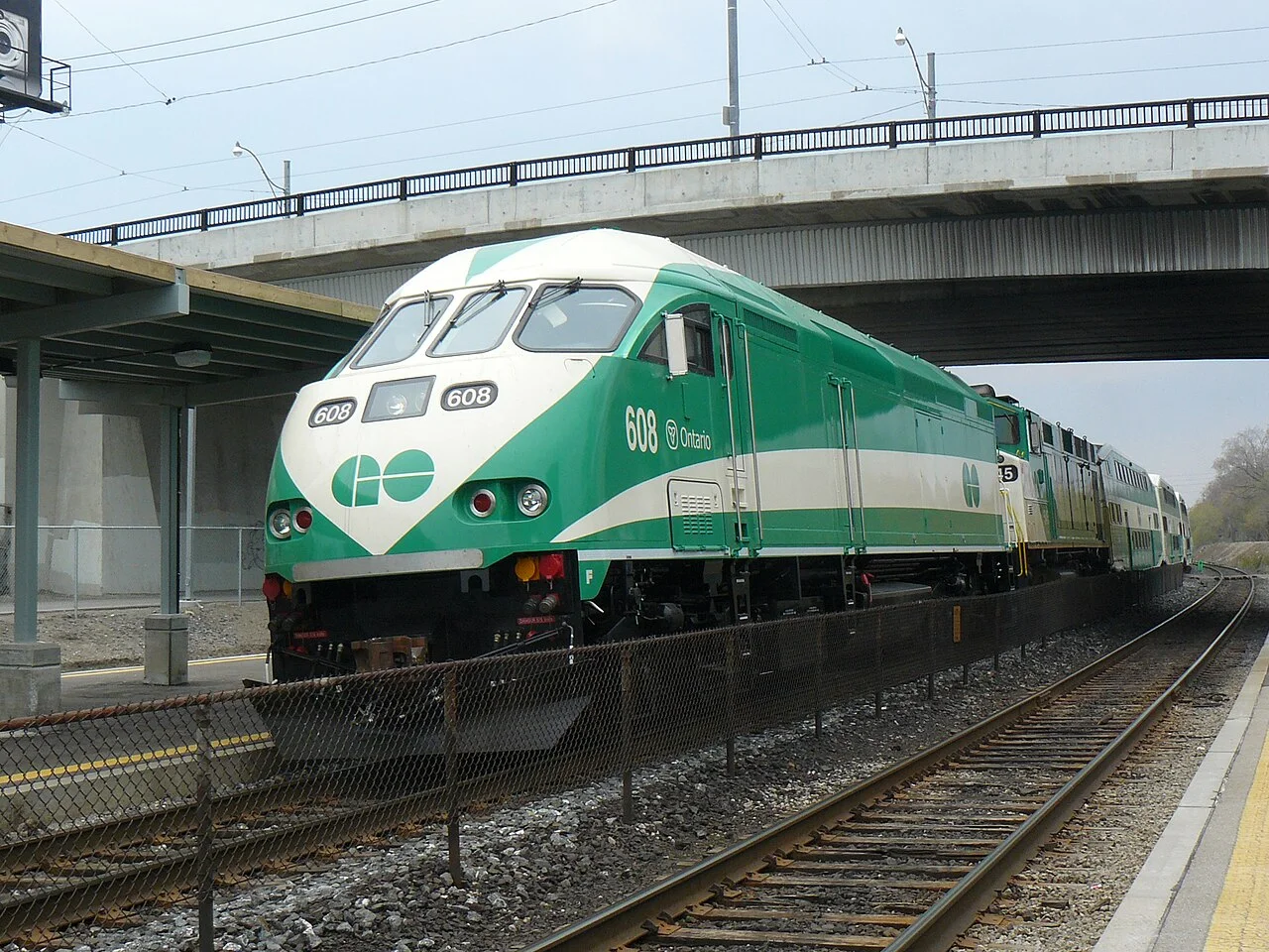 A green and white GO locomotive beside a station platform.
