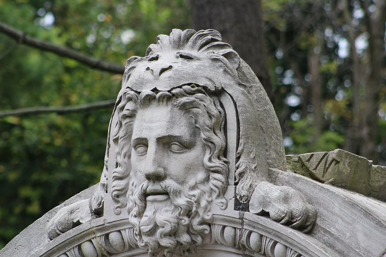 A carved bearded face and lion-head detail in stone at Guild Park.