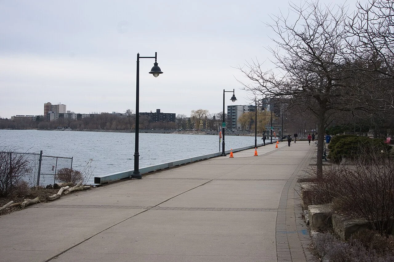 A paved waterfront promenade with lamps and walkers in Mimico.