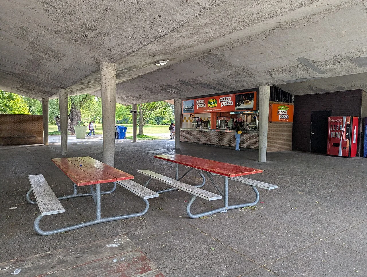 Picnic tables under a concrete shelter beside a Centre Island food concession.