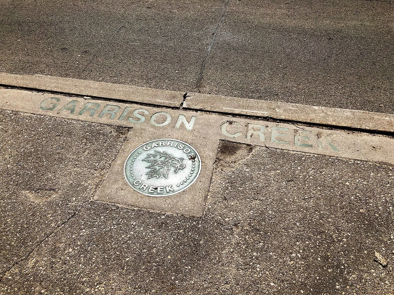 A Garrison Creek marker inset into the pavement at Trinity Bellwoods Park.