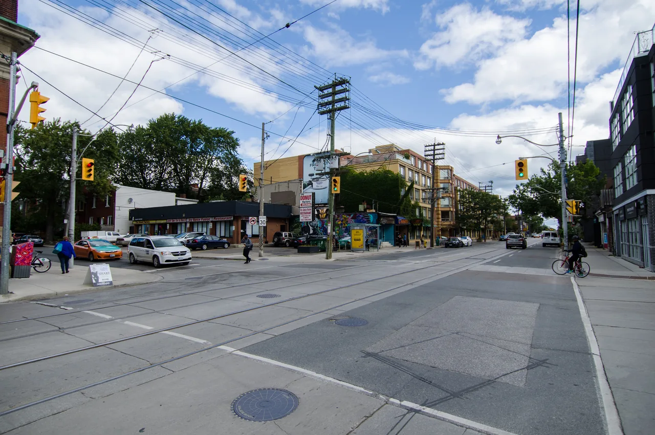 Shops, pedestrians, cyclists and streetcar tracks along Queen Street East at Boston Avenue in Leslieville.