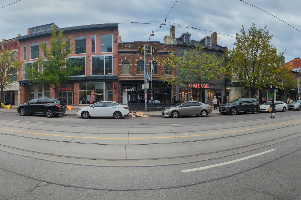 Brick shopfronts, trees and streetcar tracks along Queen Street West in Toronto.