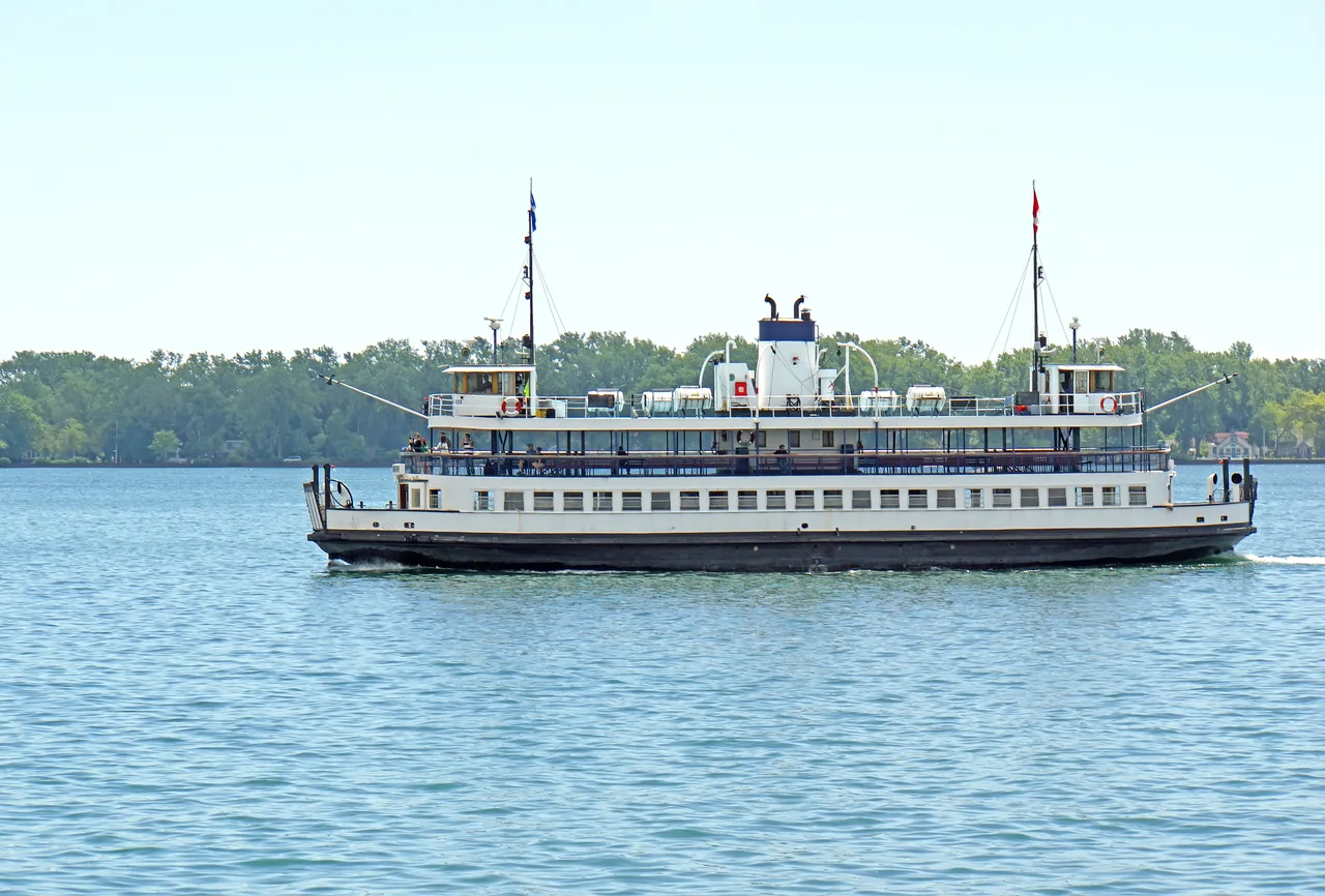 A white Toronto Islands ferry crosses the harbour in front of the wooded islands.
