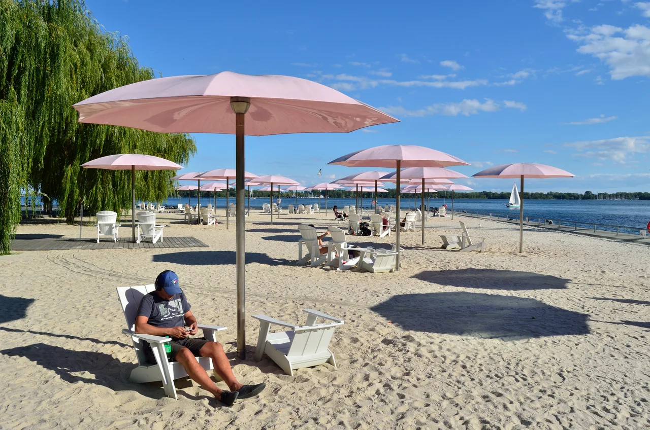 Pink umbrellas and white Muskoka chairs on the sand at Sugar Beach beside Toronto Harbour.