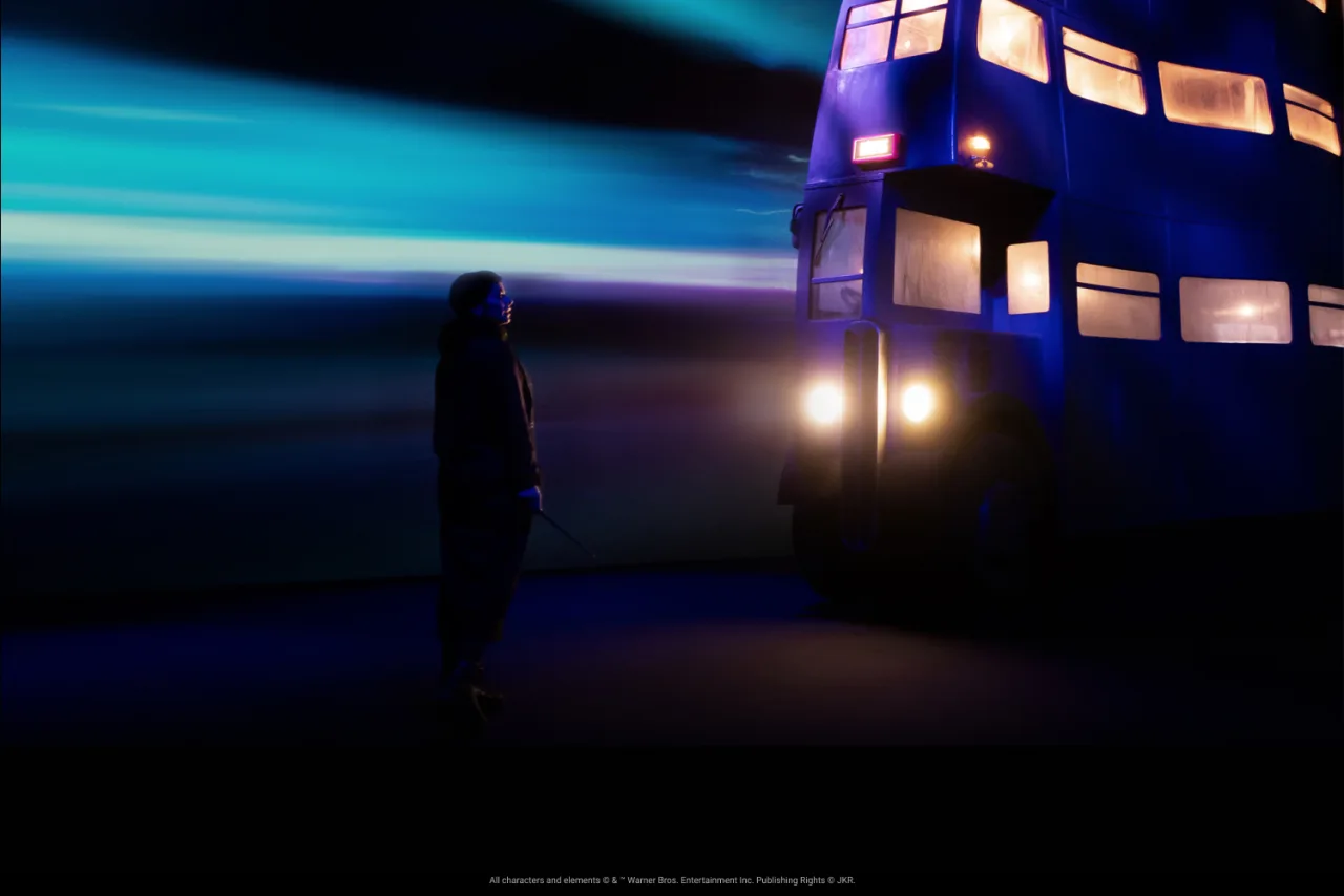 A visitor holds a wand beside the purple Knight Bus installation at Harry Potter: Visions of Magic.