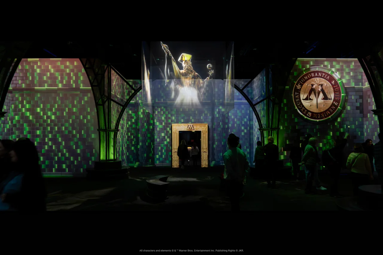 Visitors explore a green-lit Ministry of Magic environment at Harry Potter: Visions of Magic.