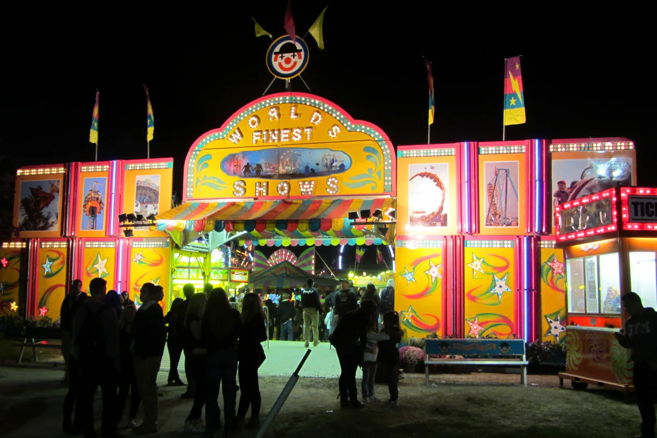 Visitors walk through the illuminated World’s Finest Shows midway entrance at Markham Fair at night.