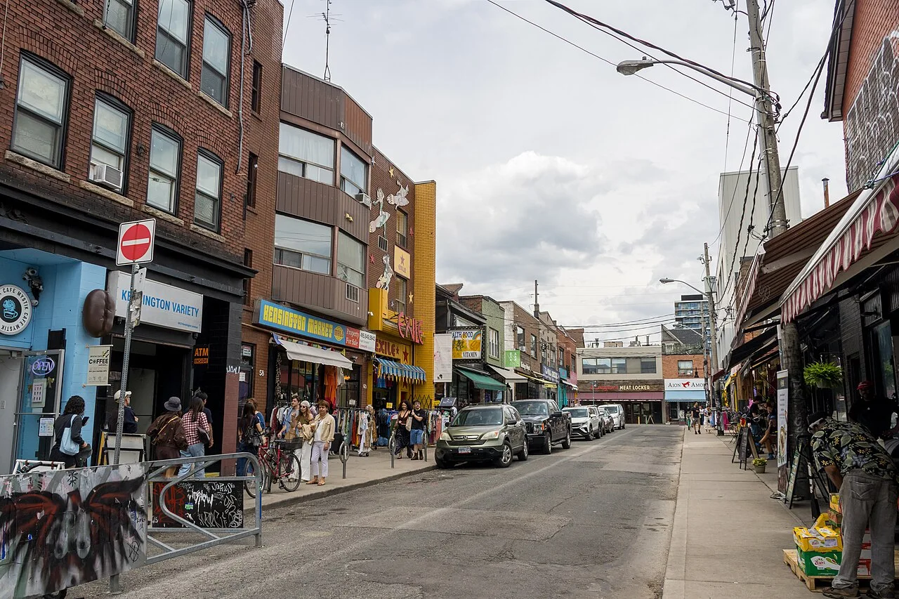 Kensington Avenue shops, pedestrians and parked vehicles under an overcast sky in June 2026.